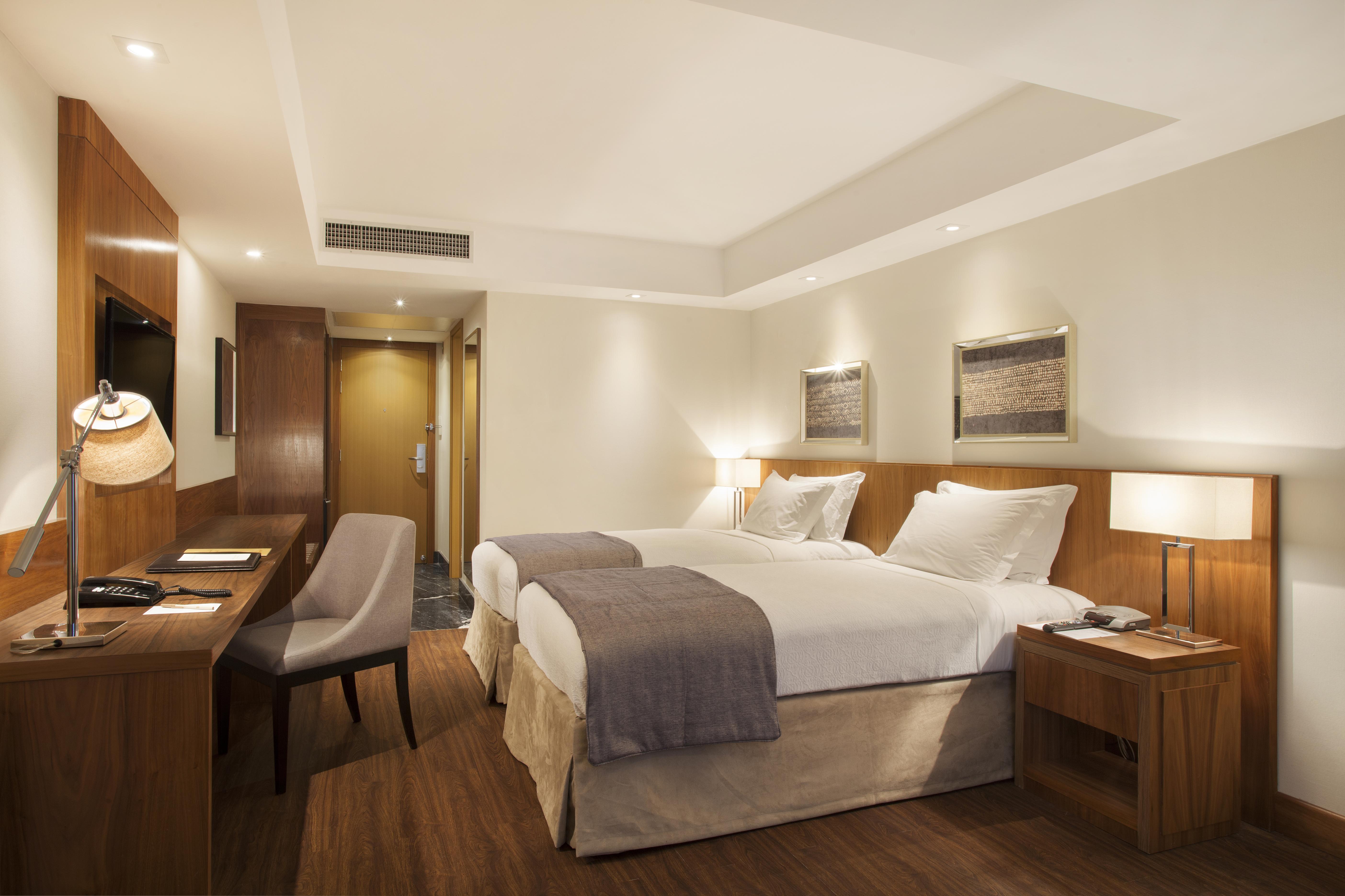 ריו דה ז'ניירו Windsor Marapendi Hotel מראה חיצוני תמונה The photo displays a modern hotel room featuring two twin beds with crisp white linens and gray throw blankets. The room has a clean and minimalist design, with wooden accents, including a bedside table and a desk. To the left, there's a small desk a
