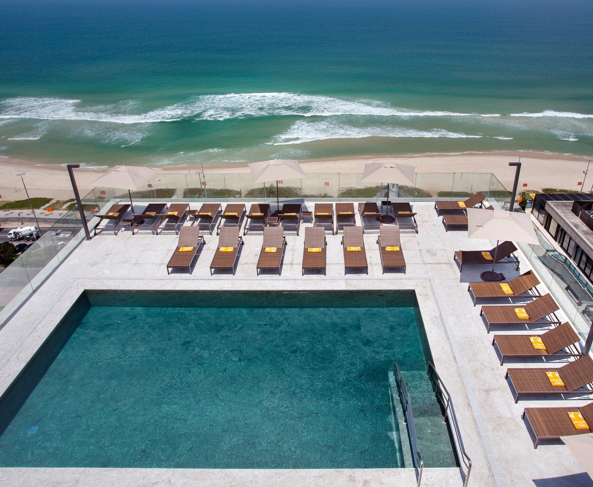 ריו דה ז'ניירו Windsor Marapendi Hotel מראה חיצוני תמונה The photo shows a rooftop area with a swimming pool and several lounge chairs arranged around it. The pool has a clear blue surface, and the lounge chairs are positioned in a neat row, some with yellow cushions. In the background, you can see a beaut