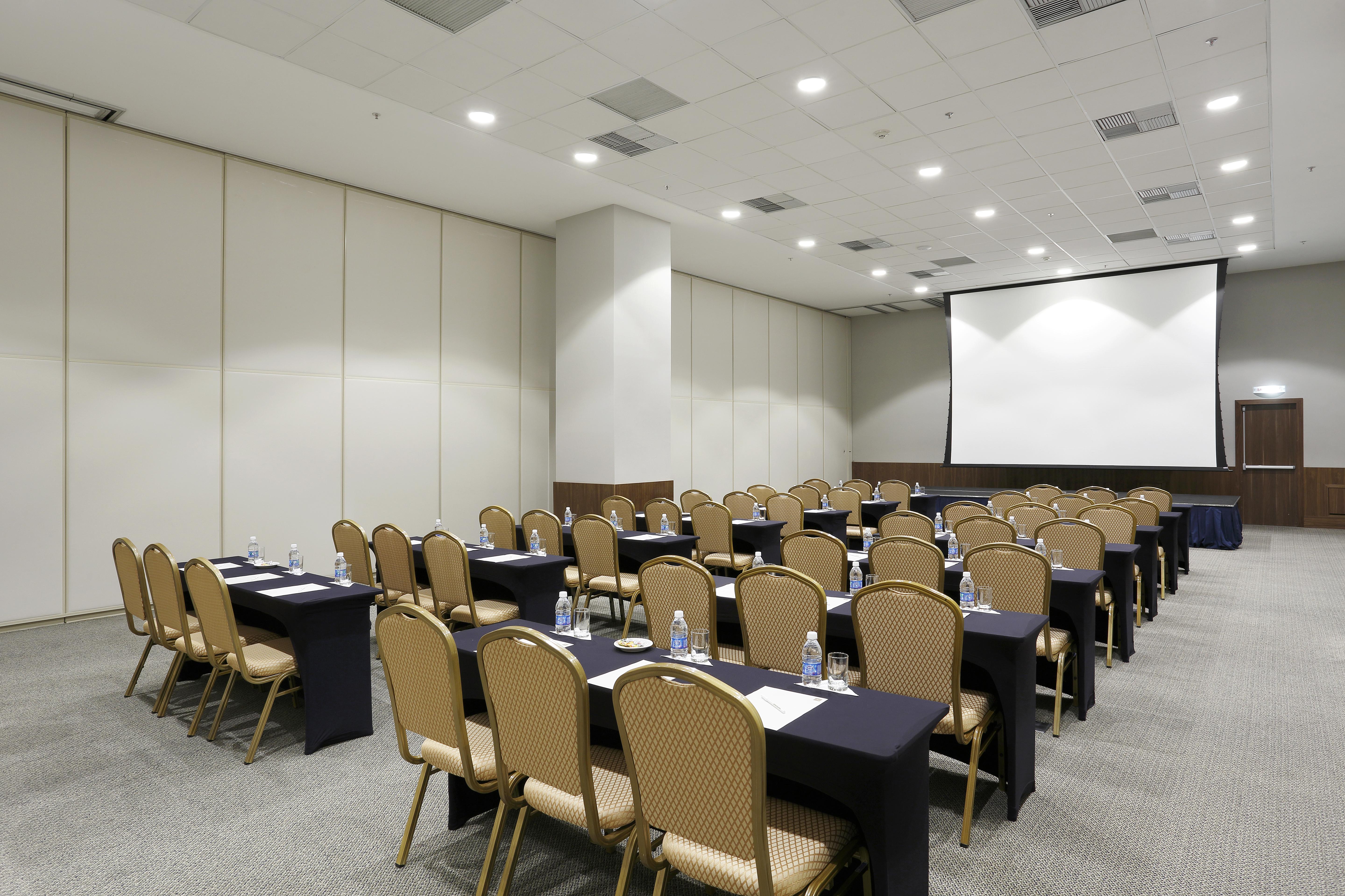 ריו דה ז'ניירו Windsor Marapendi Hotel מראה חיצוני תמונה The photo shows a conference or meeting room arranged with several rows of tables and chairs. The tables are covered with dark tablecloths and have water bottles placed on them. The room is bright and spacious, featuring a large projection screen on 