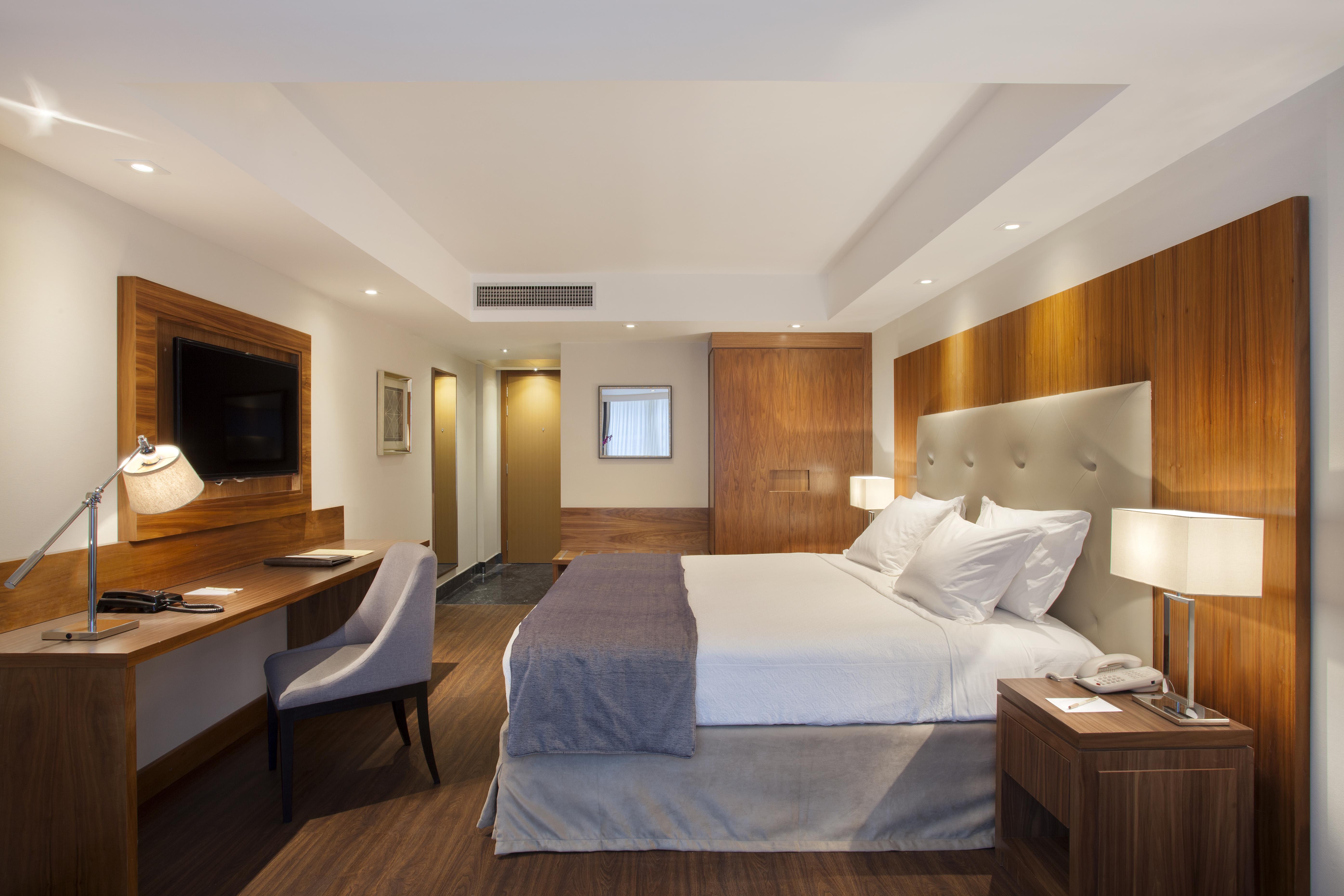 ריו דה ז'ניירו Windsor Marapendi Hotel מראה חיצוני תמונה The photo shows a modern hotel room featuring a large bed with white and gray bedding. The headboard is upholstered in light fabric. There are two bedside lamps on either side of the bed, providing warm lighting. A television is mounted on the wall o